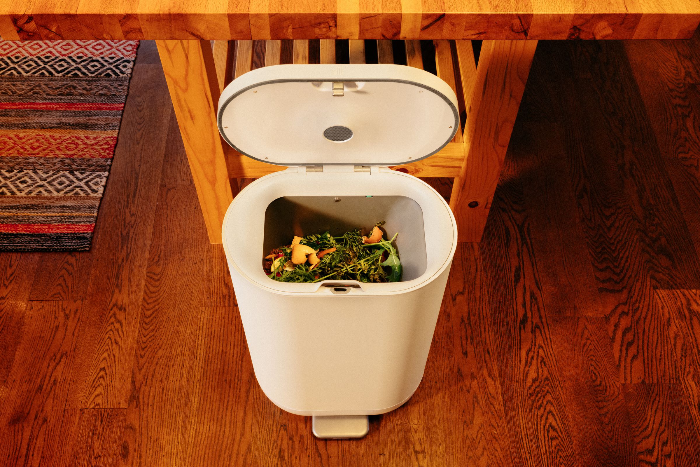 A waste bin with its lid open, showing food scraps inside.