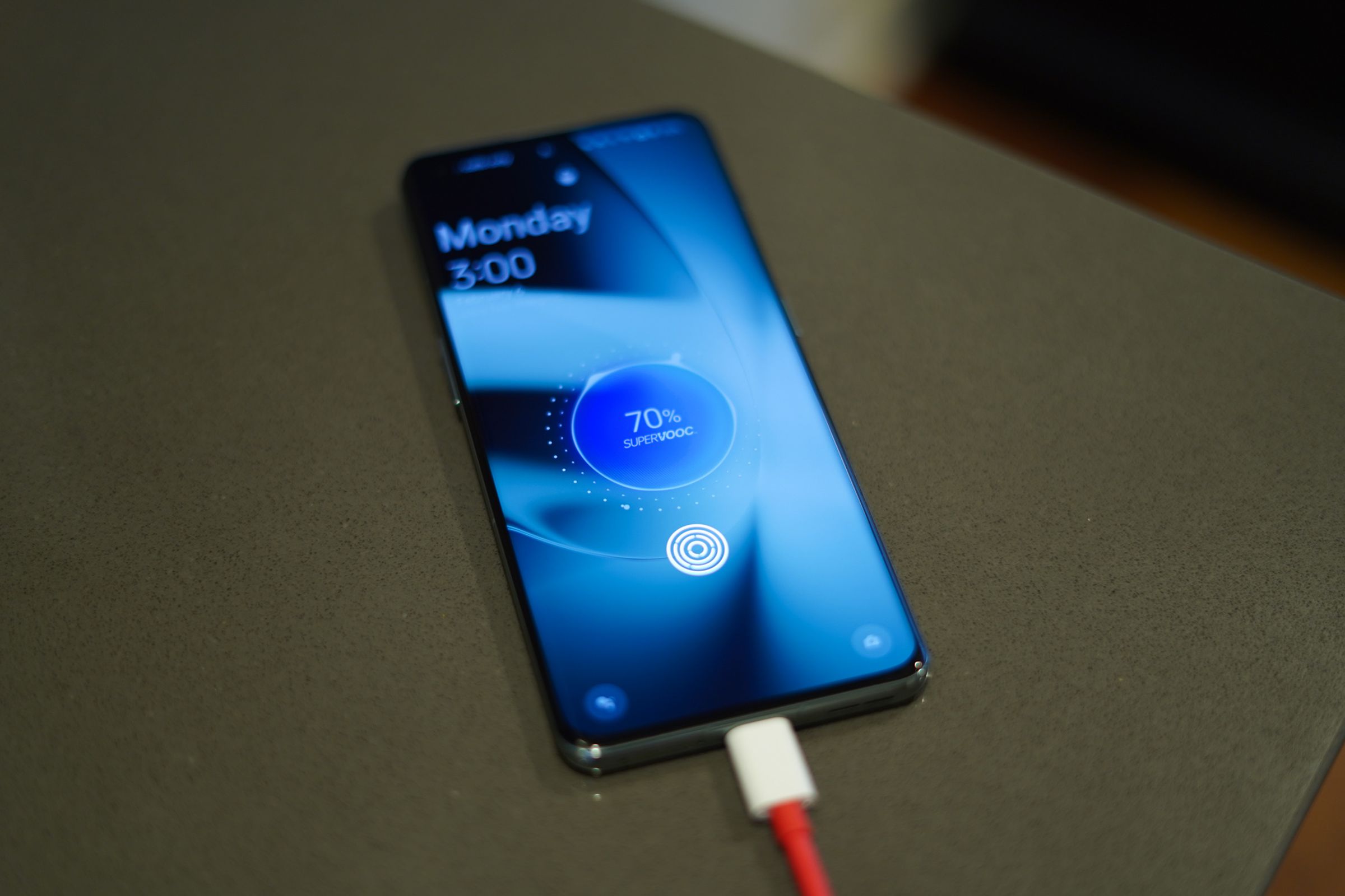 OnePlus on a countertop with screen on showing SuperVOOC fast charging logo.