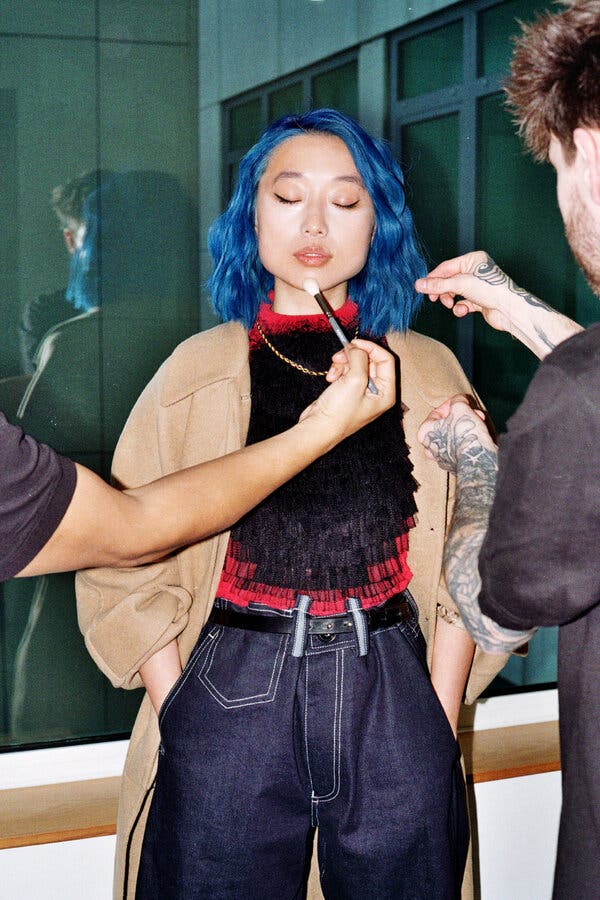 Two makeup artists attend to Ms. Zhang, one touching up her face with a makeup brush, another fussing with her hair. 