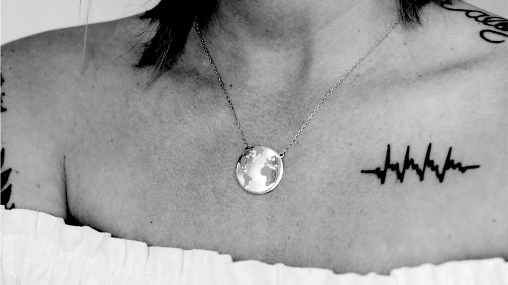 A woman wearing a necklace of the Earth and a tattoo on her upper chest
