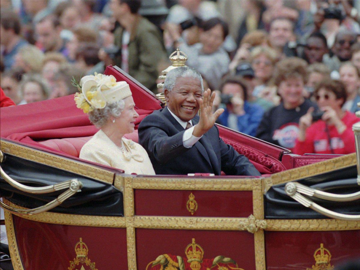 South African President Nelson Mandela waves to crowds as he sits next to Queen Elizabeth II in a an open carriage on the way to Buckingham Palace in London