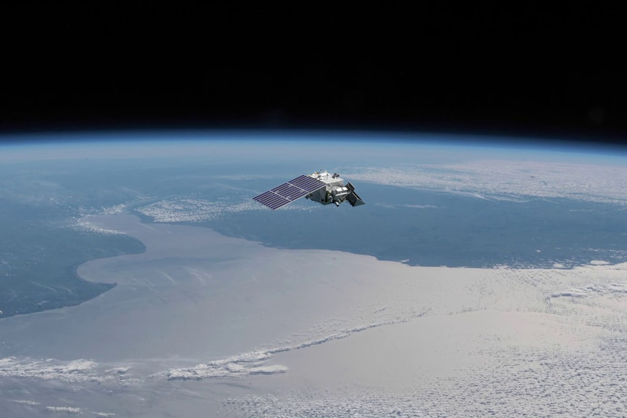 A rendering of a satellite seen above clouds, sea, and land masses.