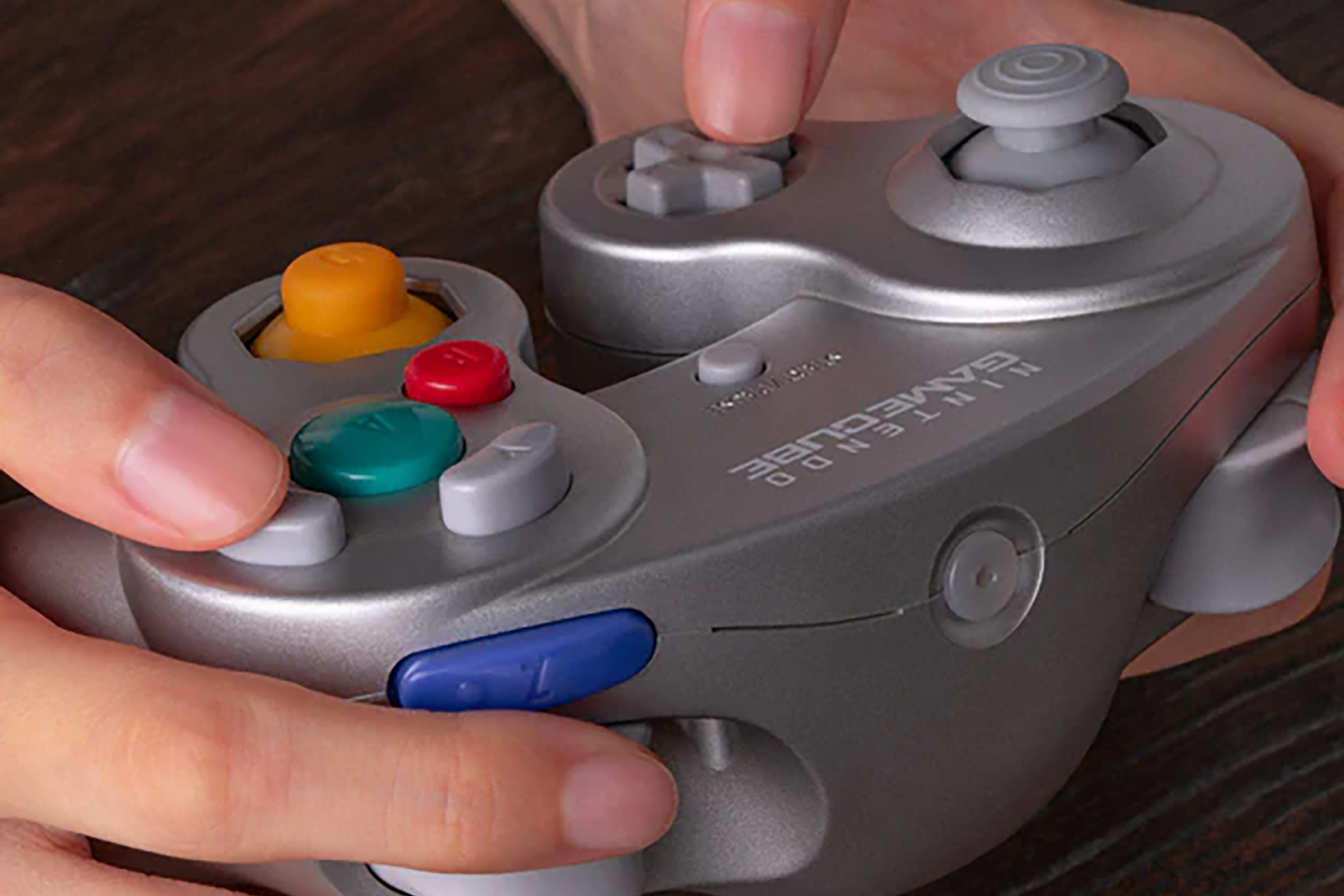 A picture of hands holding a silver GameCube controller. The area where the cable would normally protrude is now plugged.