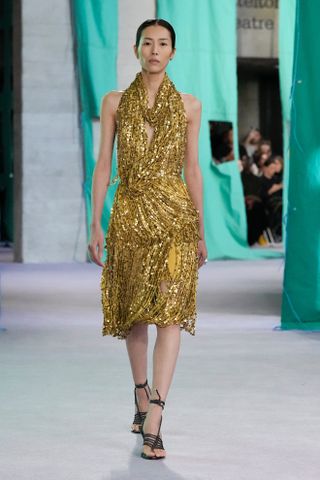 A woman wears a gold sequin midi dress with black heels.