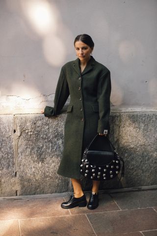 Woman in green coat and embellished bag.