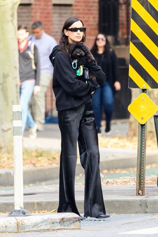 Irina Shayk wears black satin pants with a hoodie while holding her dog