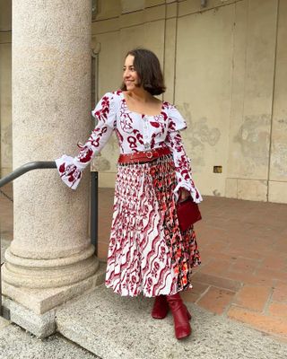 Editor in Chief Hannah Almassi wears a red and white printed dress with red boots standing near a limestone pillar