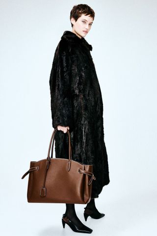 Woman in faux fur coat carries brown tote bag