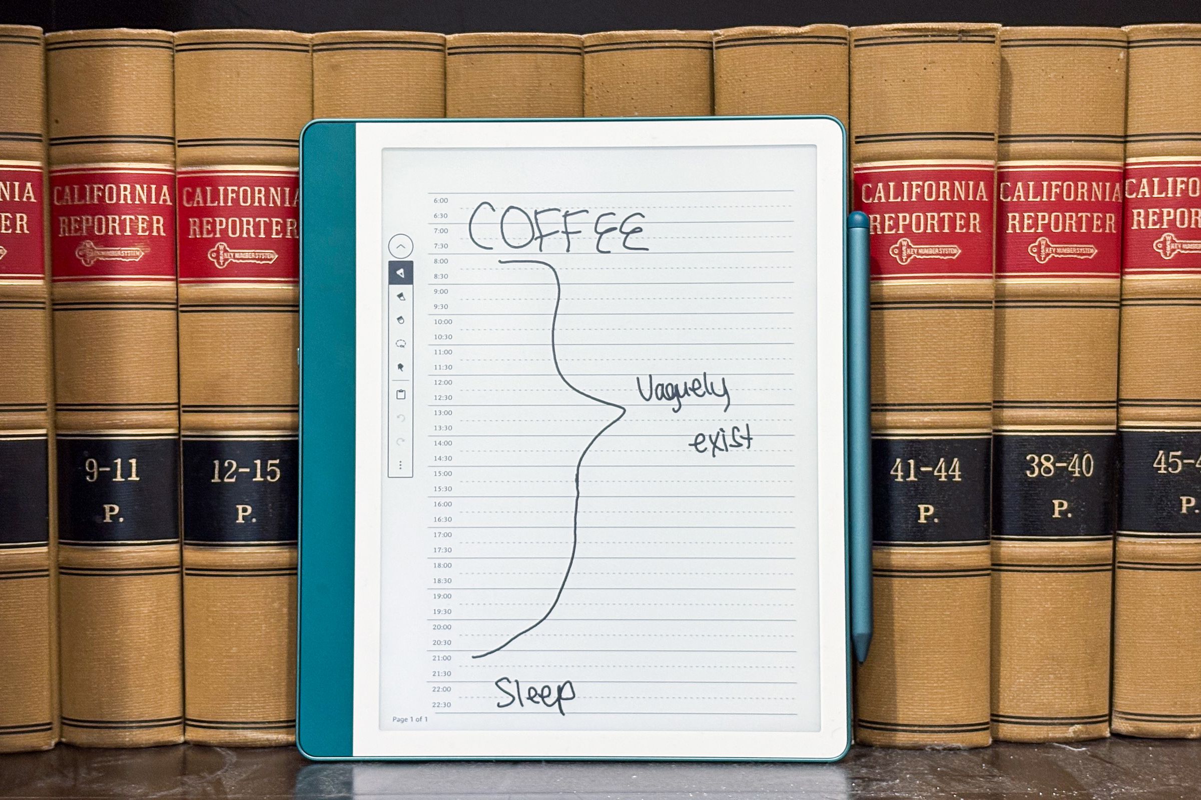 The Kindle Scribe resting against a bookshelf with a notebook page opened up to a daily planner.