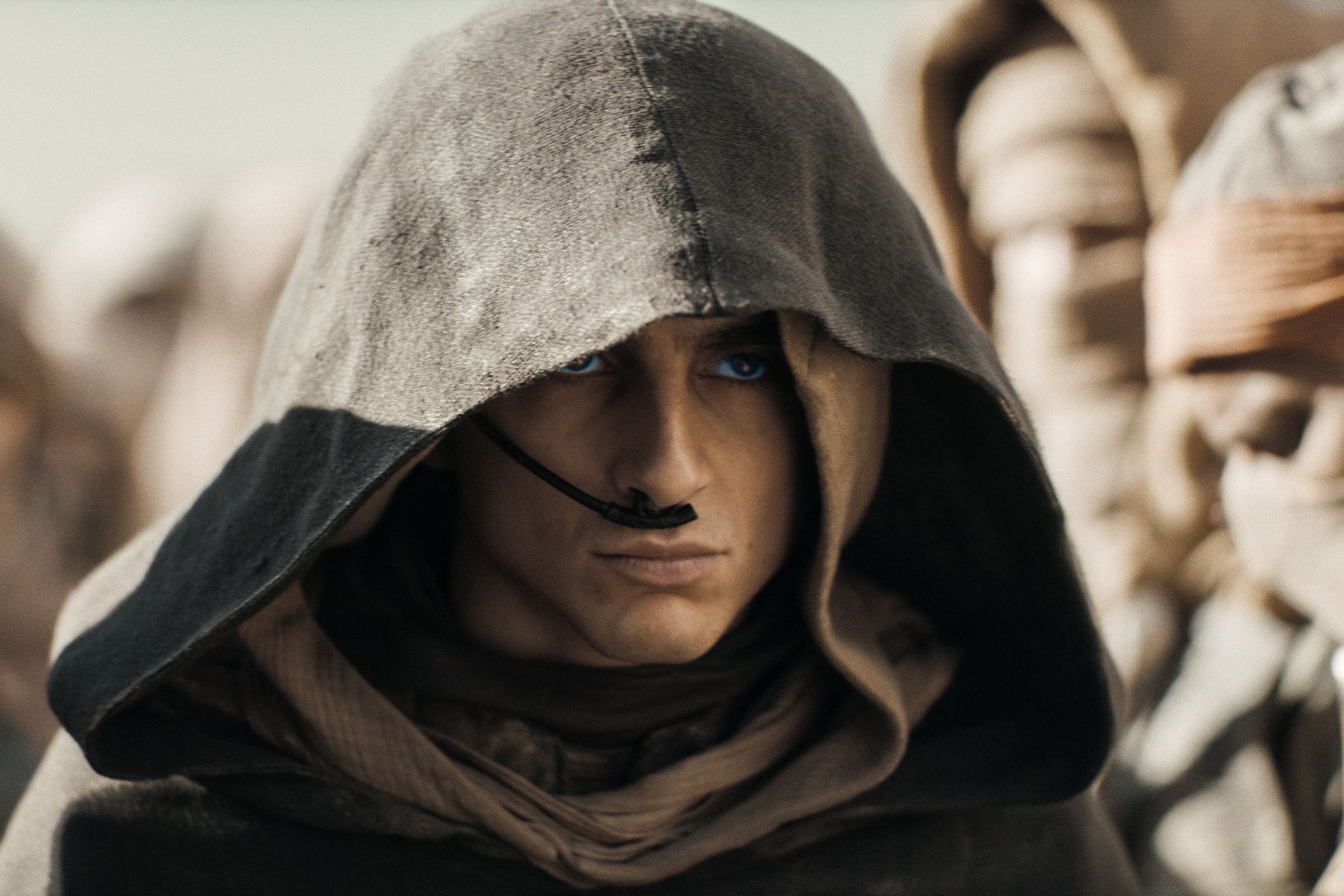 A tight shot of a hooded and cloaked man wearing with a thin breathing apparatus wrapping around the side of his face.