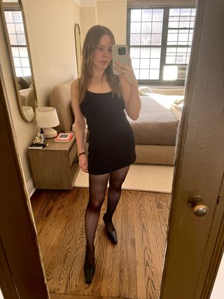 Nikki wears a black tank top and a black skirt with tights and pumps