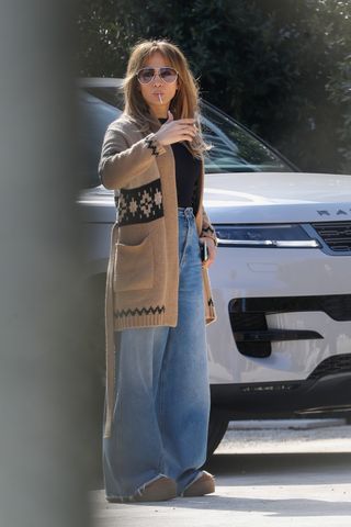 Jennifer lopez wears a black top, fair isle sweater, wide-leg jeans, and ugg boots.