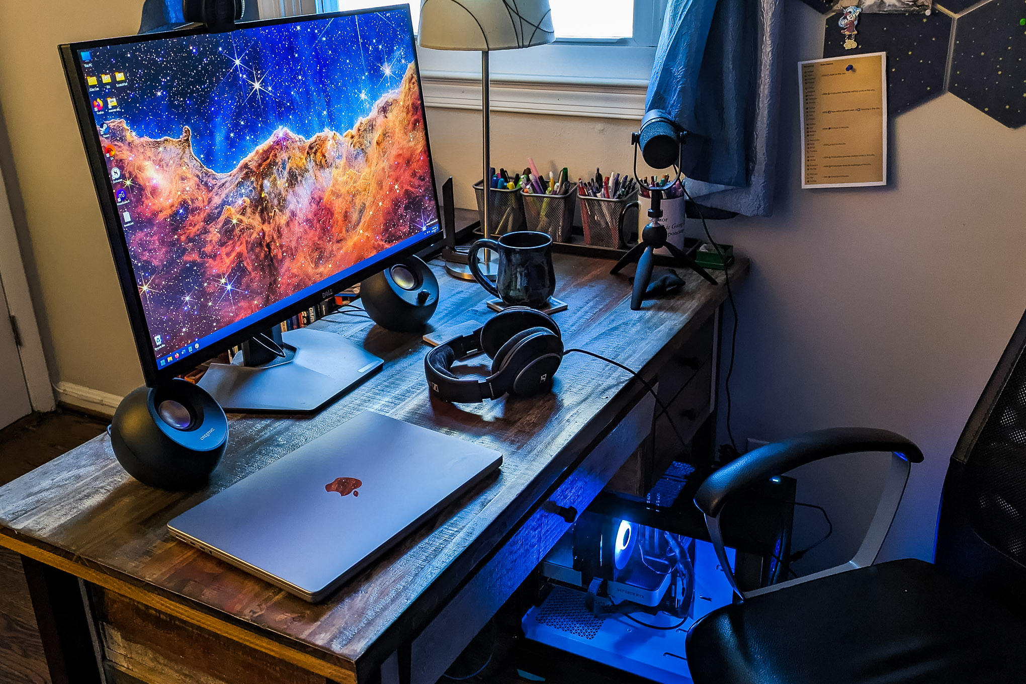 A work desk with a monitor, an Apple computer, and a pair of headphones, next to a window.