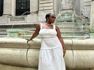 Aniyah wears white dress and white fisherman sandals while posing in front of a large fountain