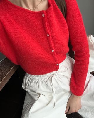 Woman wears red cardigan and white trousers