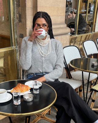 Woman wears grey cardigan, pearl necklace and black jeans