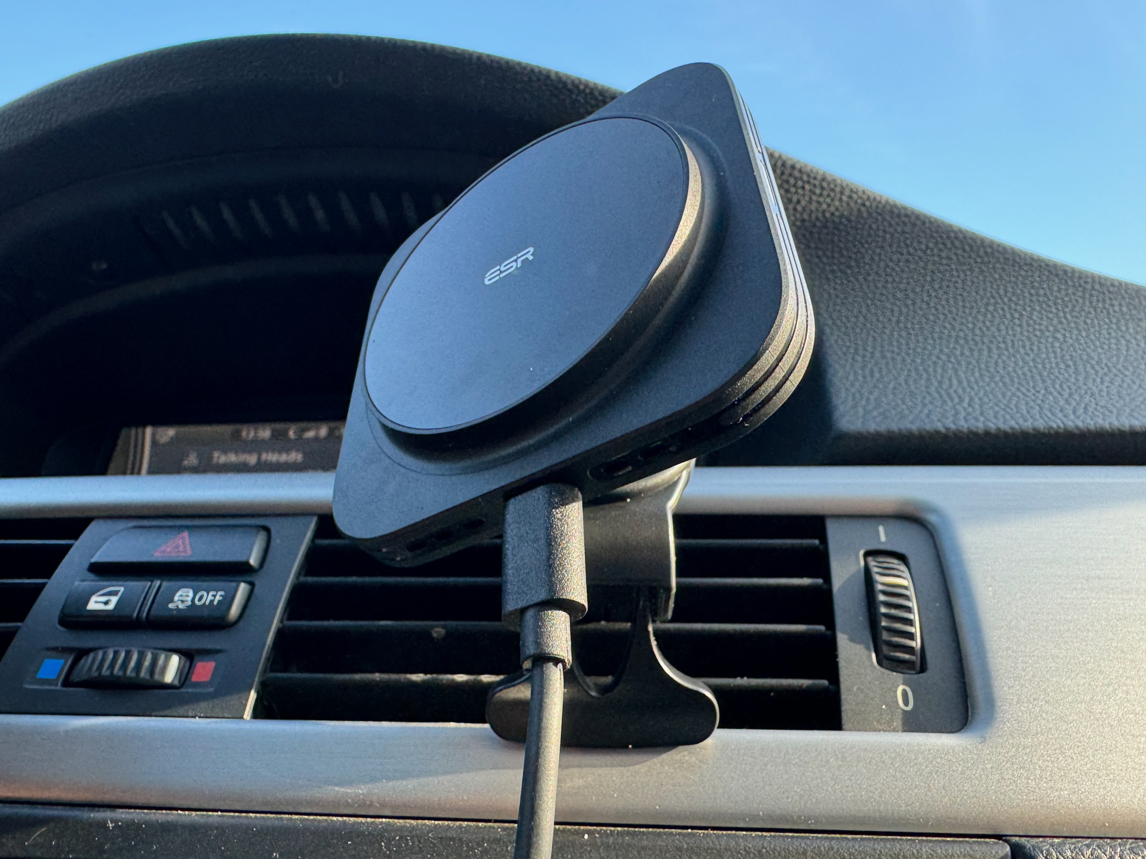 A black plastic car charging mount with the ESR logo at the center of the circular charging puck is mounted to a car’s vent.