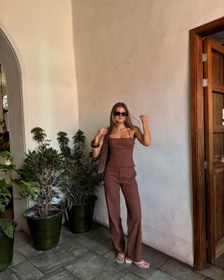 Sara wears a brown linen top, brown linen pants, and white sandals.
