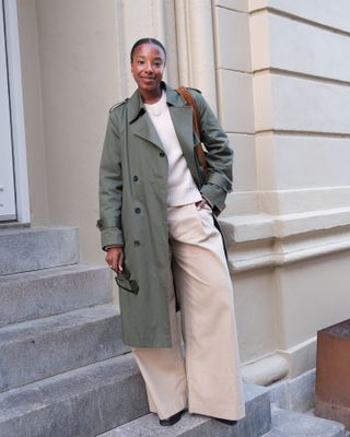 Taffy wears a green trench coat, white sweater, and beige pants.