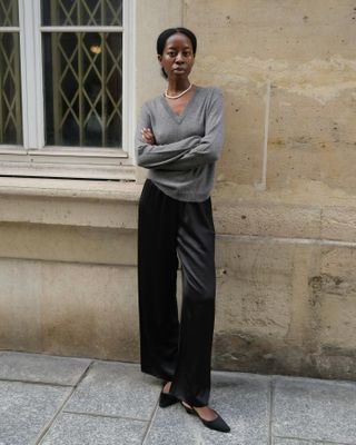 Sylvie wears a gray sweater, black silk pants, and black flats.