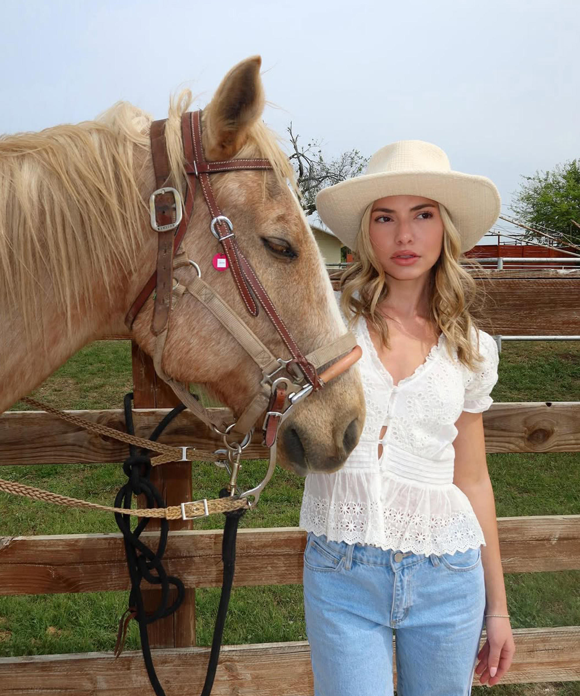 Kit Keenan poses with a horse in a cream cowboy hat, white blouse, and blue jeans
