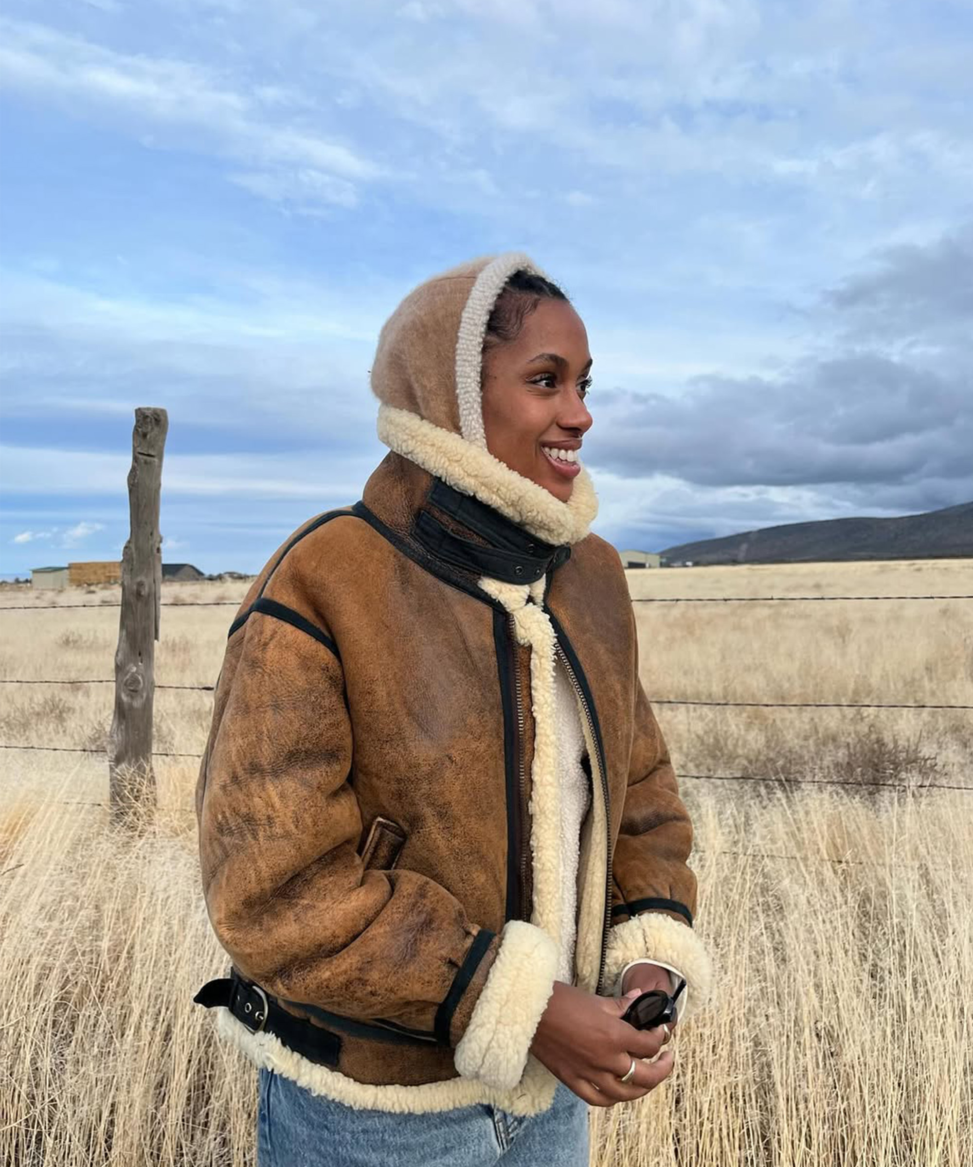Claire Most smiles while wearing an oversized leather jacket in a field