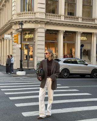 Fashion influencer @fredrika_ekerot in New York wearing an "anti-trend" outfit styled with belted creamy baggy jeans, relaxed blazer, brown top, and brown suede flats.