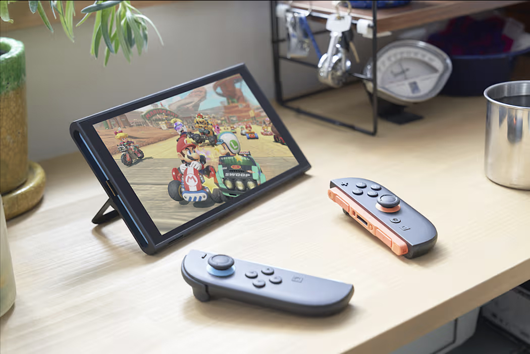 The Nintendo Switch 2 with a Mario game playing, display on, and Joy-Cons nearby on a desk.