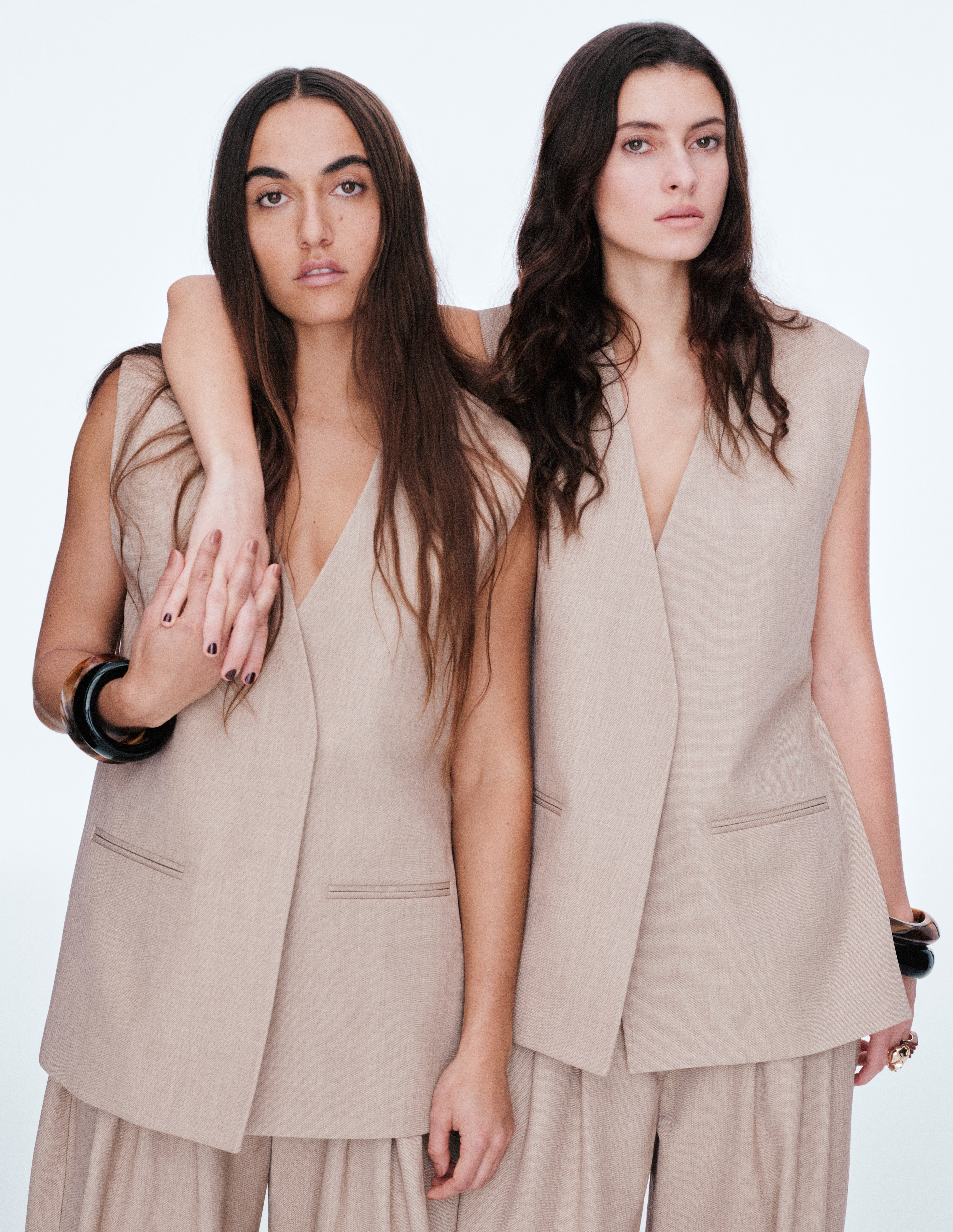 Two women wear beige waistcoats and tailored trousers