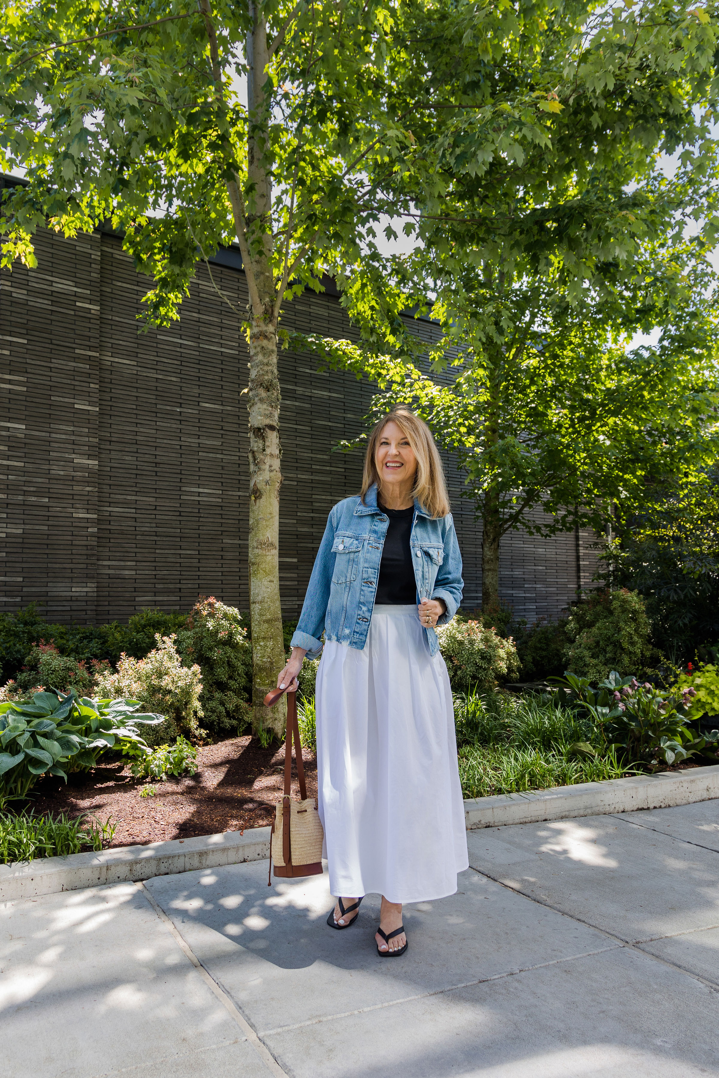 A former VIP Nordstrom stylist wearing a denim jacket, black tee, white skirt, and black flip-flops.