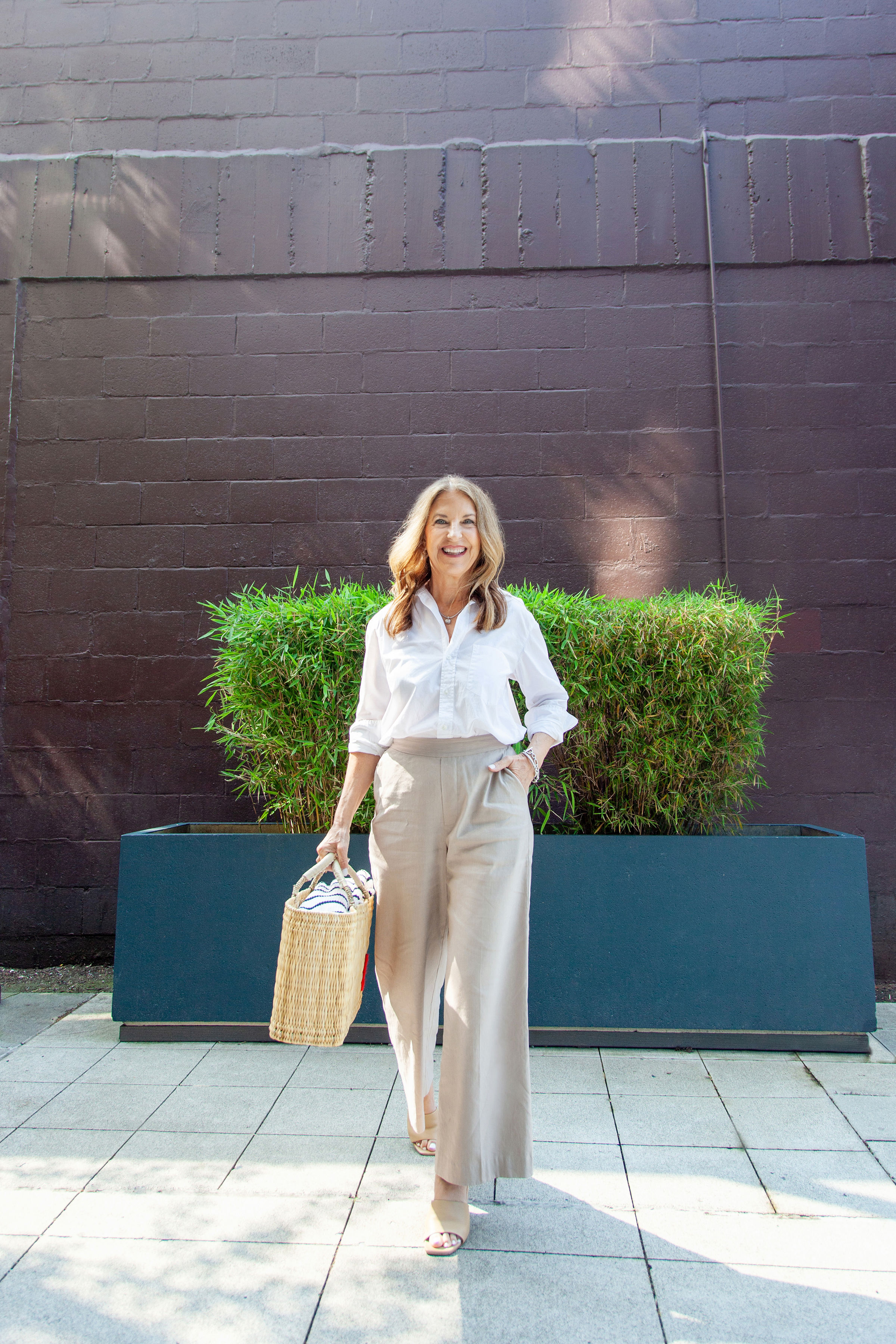 A former VIP Nordstrom stylist wearing a white button-down, tan trousers, and tan heeled sandals.
