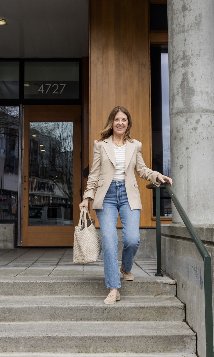 A former VIP Nordstrom stylist wearing a tan blazer, a white tee, jeans, and tan boat shoes.