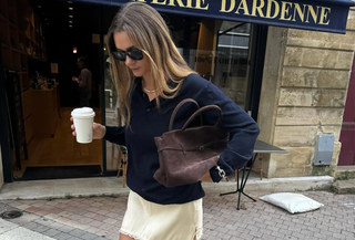 Anne-Laure Mais wearing a navy polo with a butter yellow skirt and a brown suede bag.
