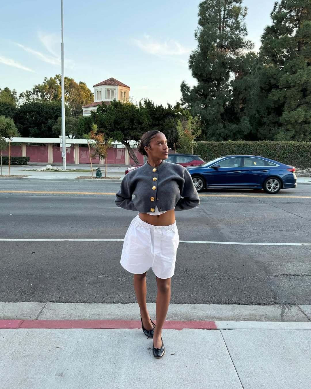Woman wearing cardigan with white boxer shorts and ballet flats in a summer 2025 outfit.