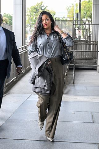 Rihanna wears trousers, a button-down shirt, and snake-print shoes.