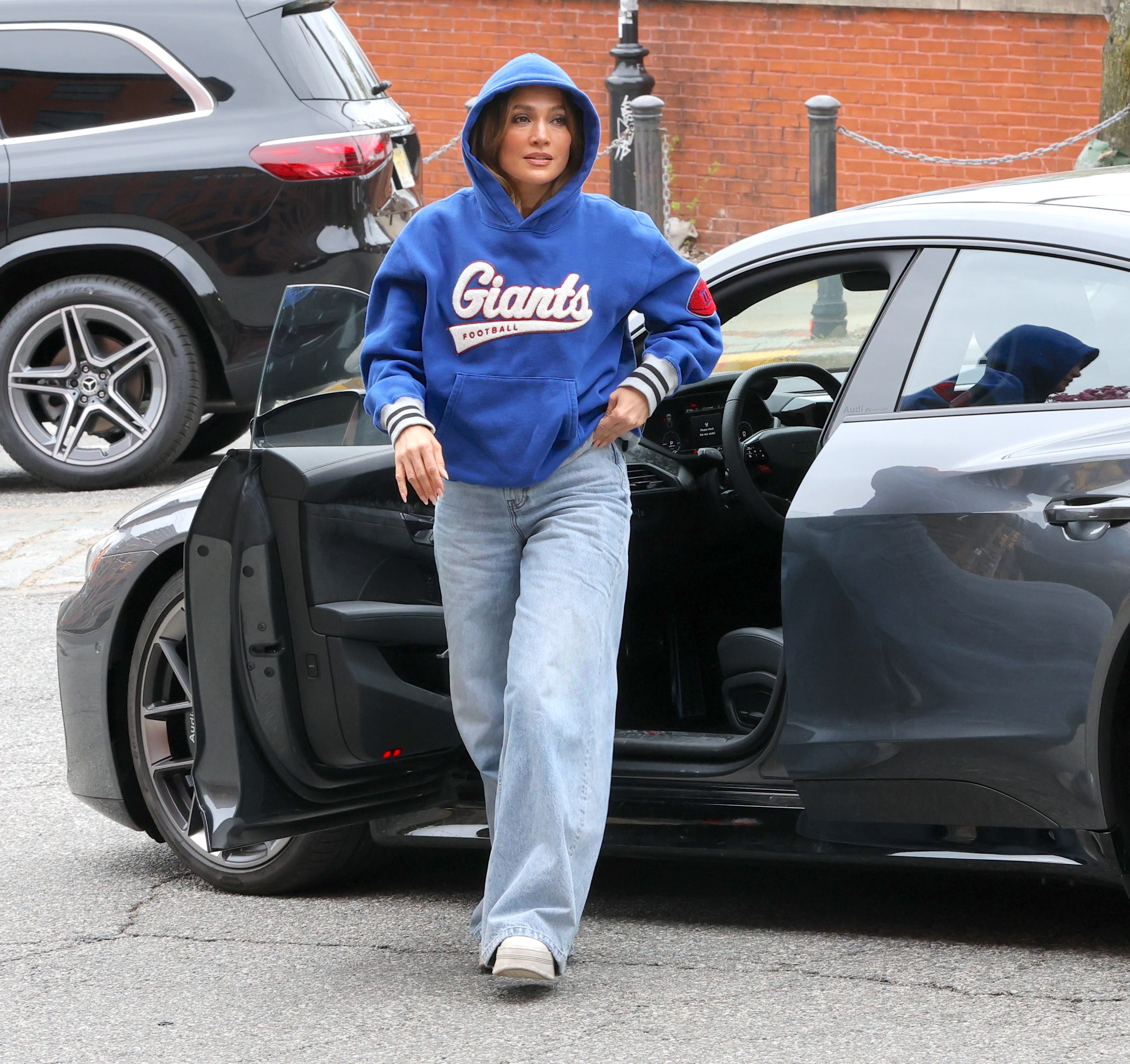 Jennifer Lopez wears a blue Giants sweatshirt, light-wash wide-leg jeans, and white sneakers.