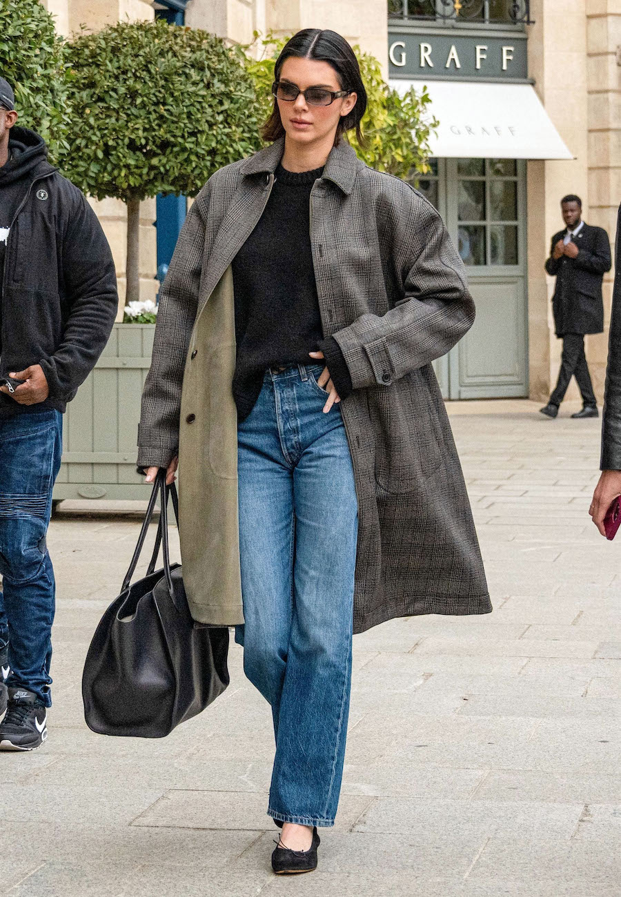 Kendall Jenner walking in Paris wearing a trench coat, black sweater, The Row bag, jeans, and black suede ballet flats