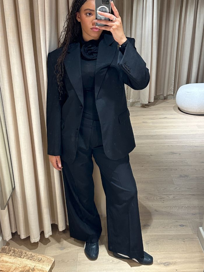 Woman wears black blazer, black top with floral appliqué and black trousers