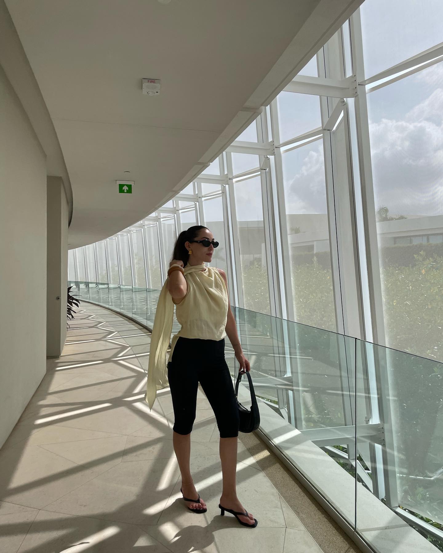 Anna wears a yellow blouse, black capri pants, and thong heeled sandals.