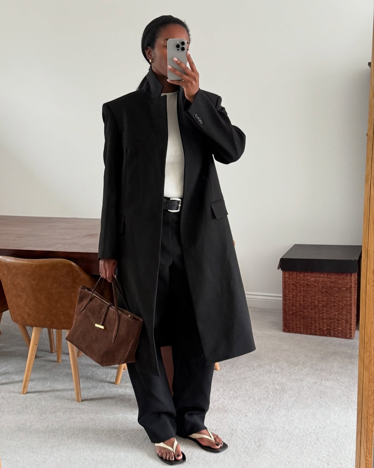 Marilyn wears a black coat, white tee, black pants, white sandals, and a brown suede bag.