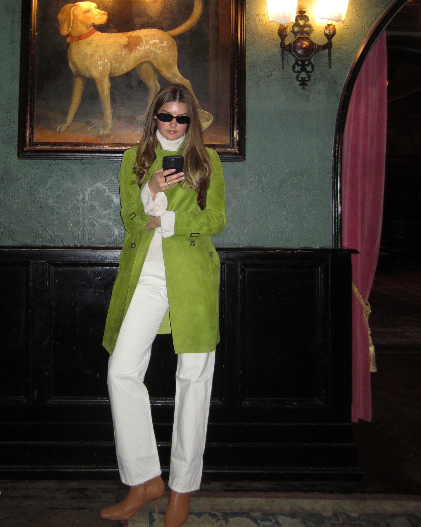 Sara wears a green jacket, white sweater, white pants, and tan boots.