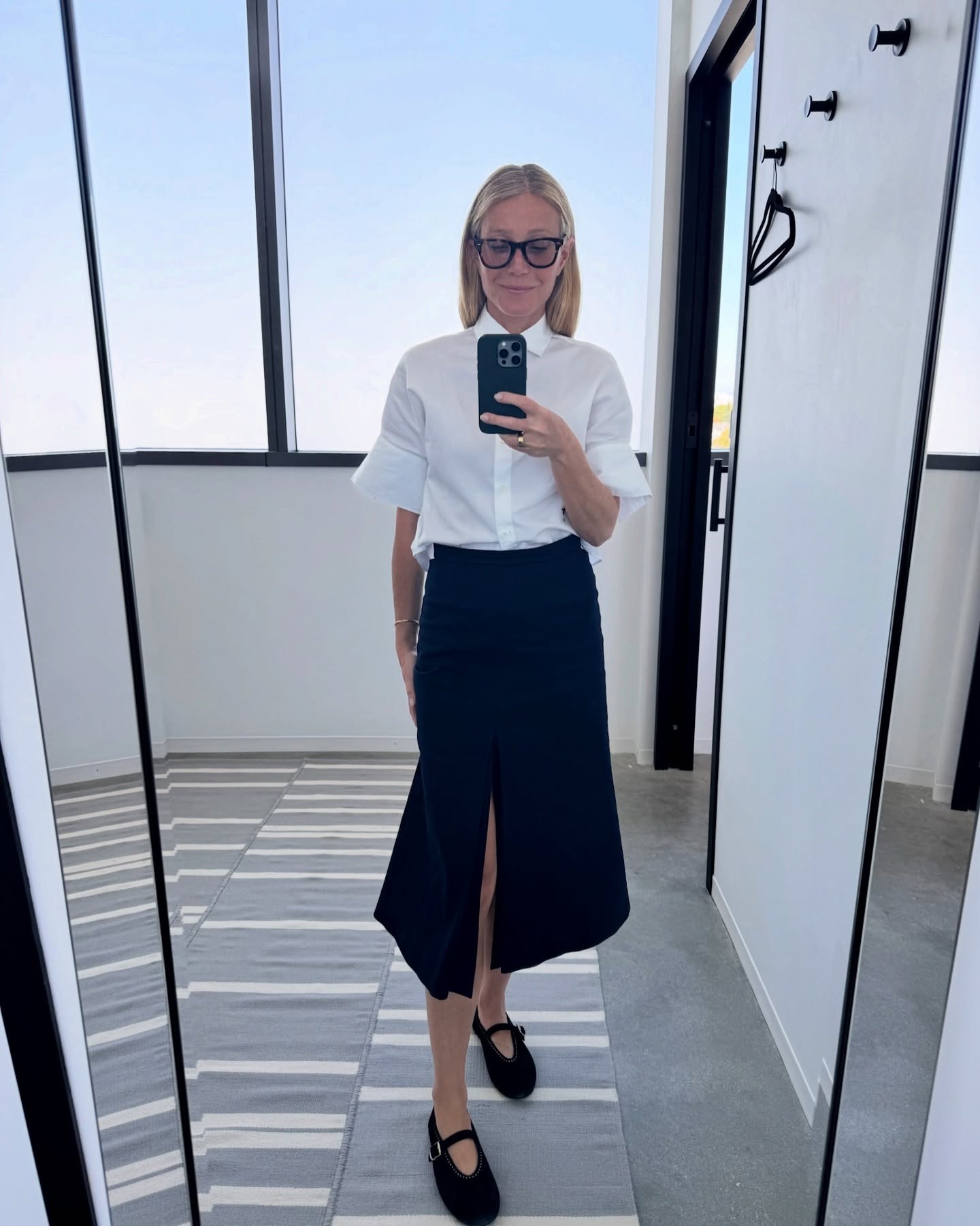 Gwyneth wears a white blouse, black midi skirt, and black mary jane flats.