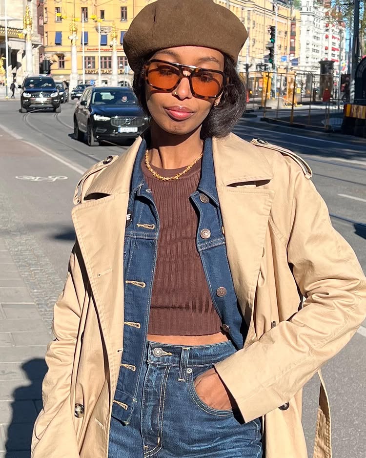 Stockholm Fashion Trends 2025: @monamali_ wears tinted sunglasses, a trench coat and a denim jacket with matching jeans