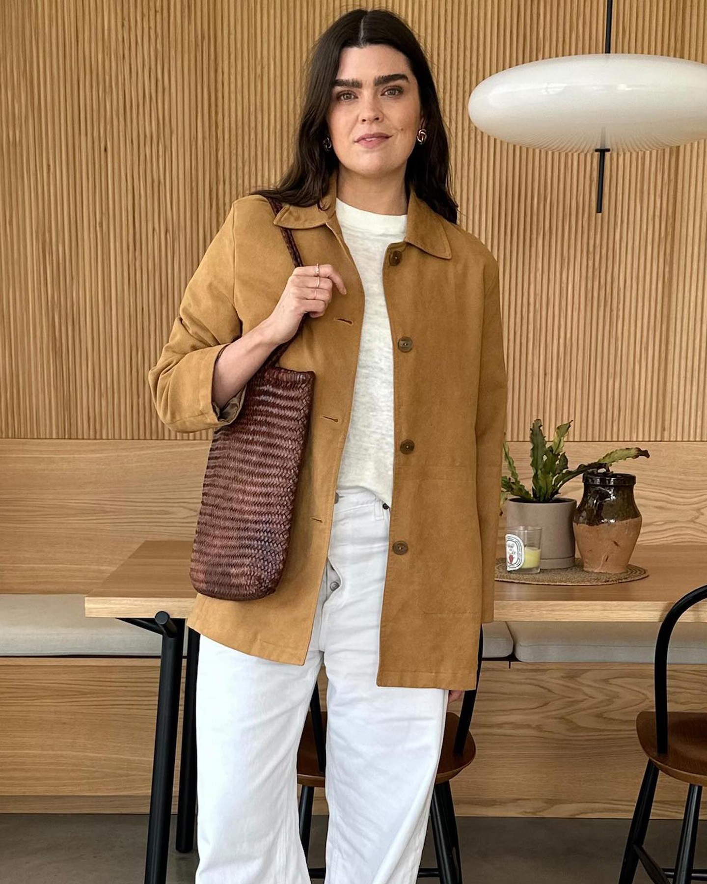 British style influencer Anna Newton wears a tan suede jacket, faded ivory linen tee, brown woven leather tote bag, and white jeans