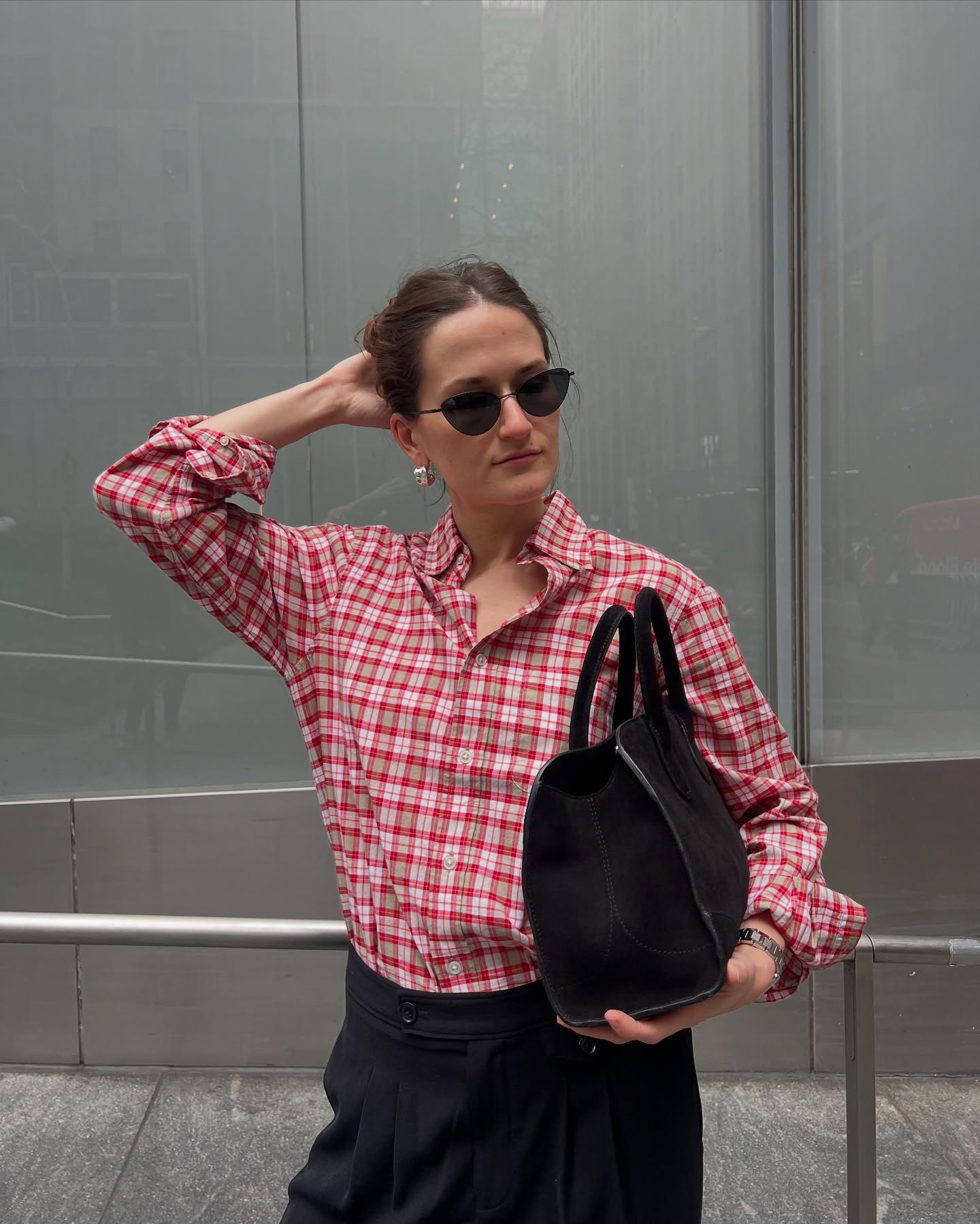 Eliza Huber wearing a red plaid shirt, black pants, and a black suede COS bag.