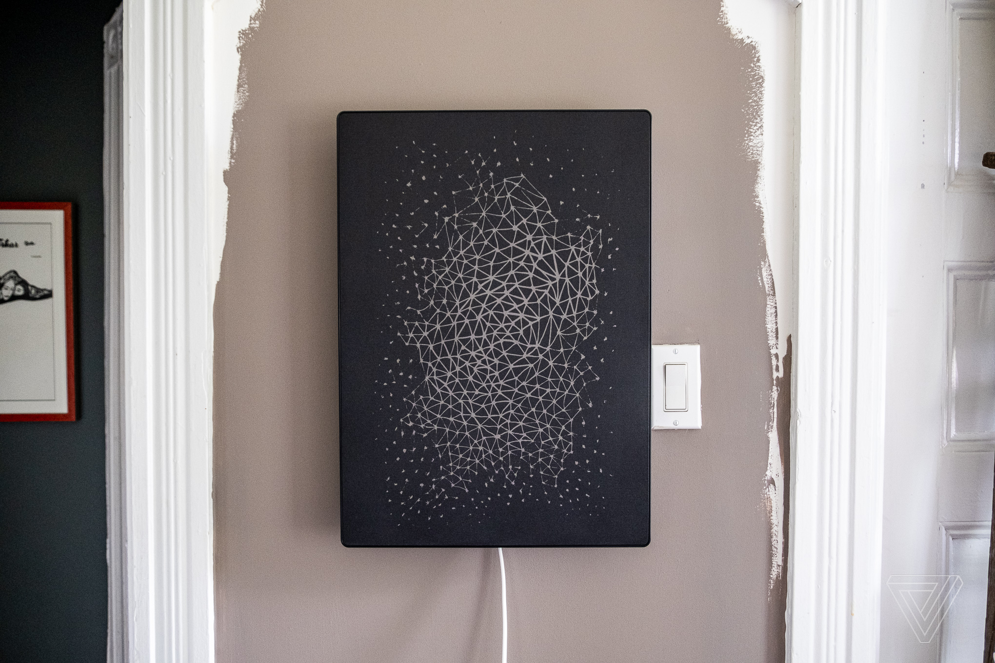 A black Ikea picture frame speaker with a geometric pattern design mounted on a wall beside a light switch.