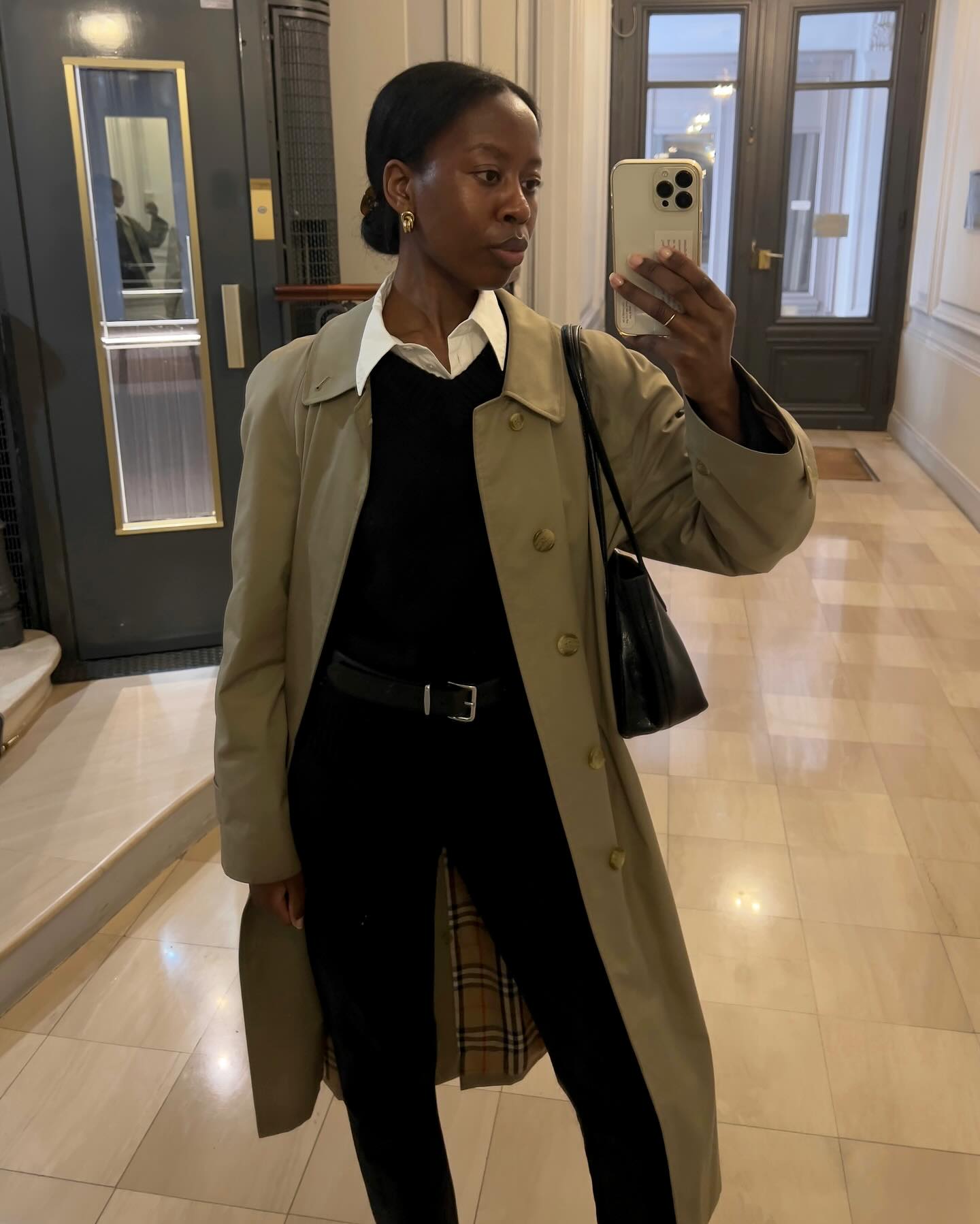 Sylvie Mus wearing a Burberry trench coat, black sweater, and black jeans.