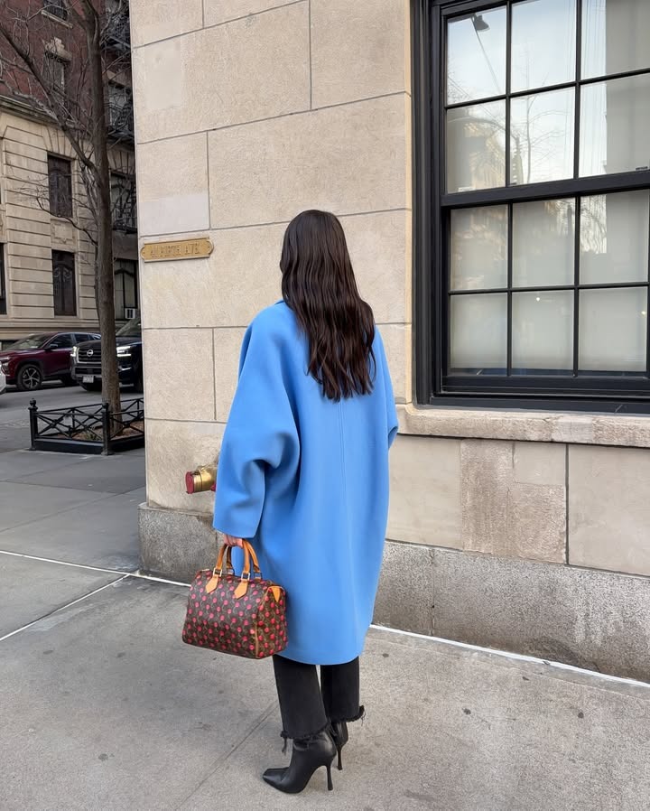 Woman turned away from the camera wearing a long blue coat and her dark hair worn down behind her shoulders.