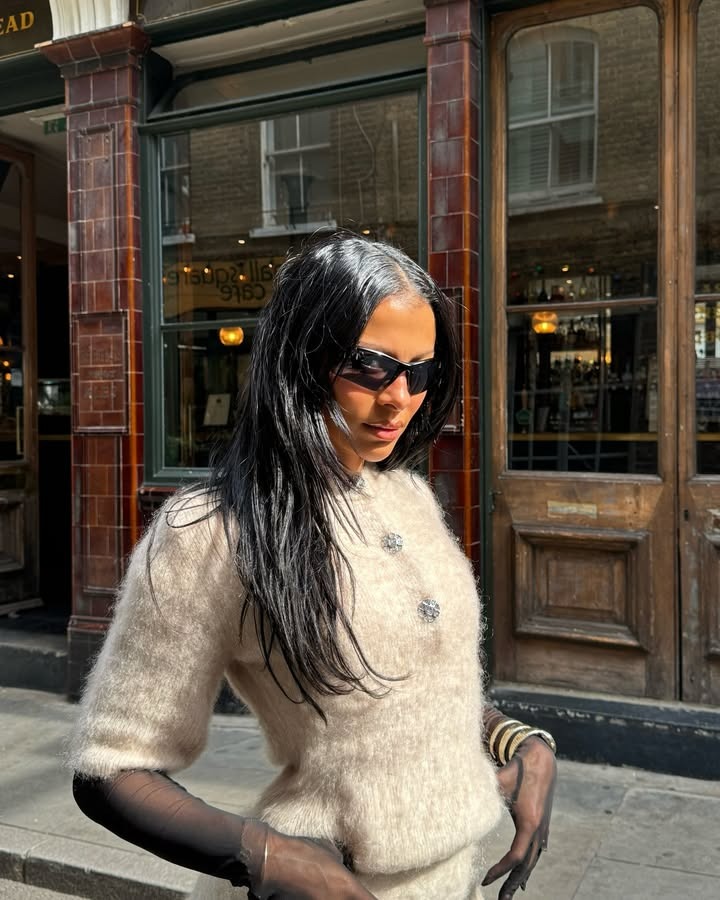 Woman wearing a fuzzy sweater set, mesh gloves, and sunglasses with her straight hair falling freely.