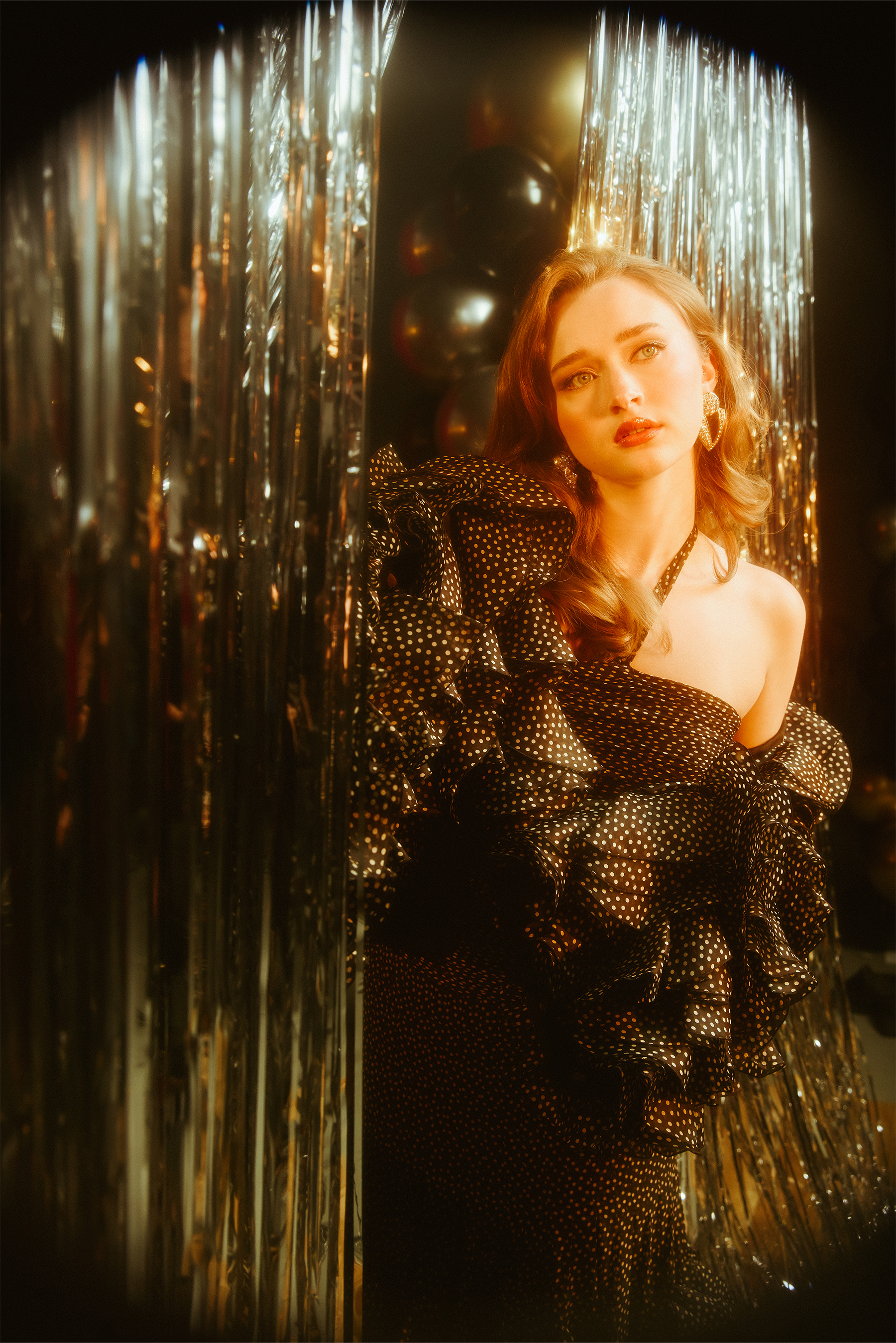 Actress India Fowler from Fear Street: Prom Queen coming through a silver tinsel wall wearing a Valentino black polka-dot gown with halter neck and ruffle detailing.